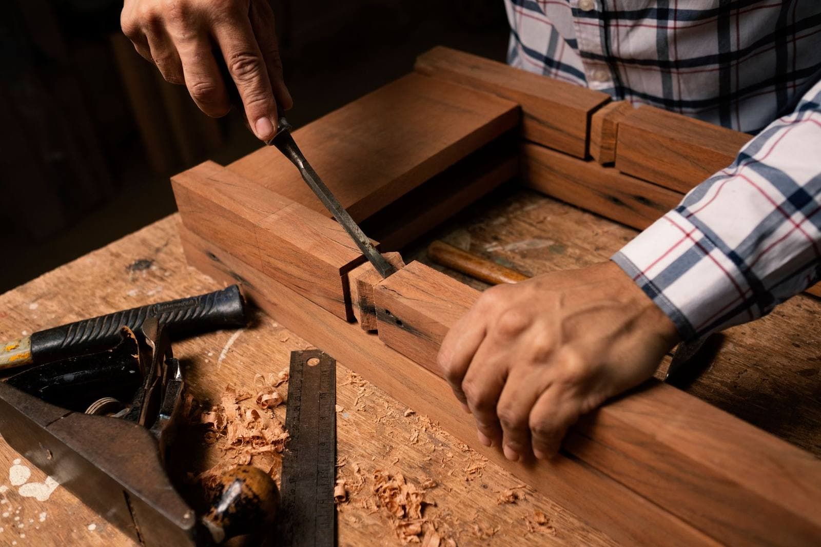 A person using a chisel on a piece of wood at a workbench