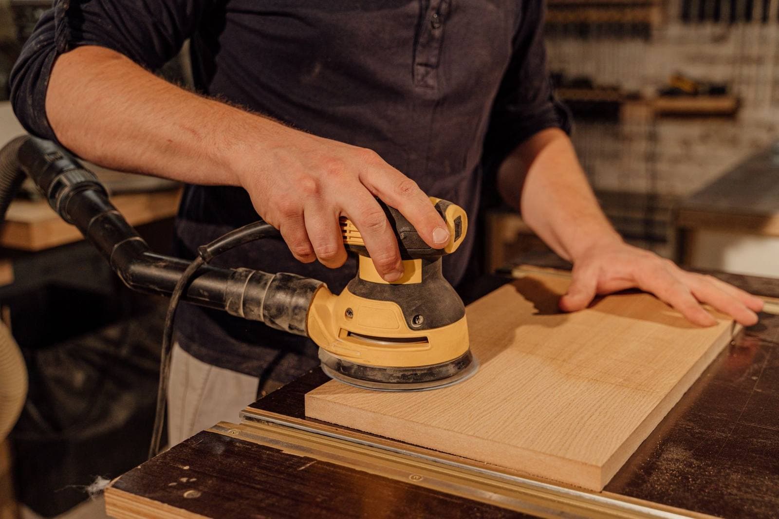 A woodworker sanding a board with a random orbital sander